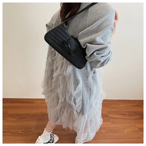 Detail view of woven black underarm bag featuring an elegant leather bow decoration
