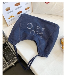 Detail of a large navy denim tote bag with white letter embroidery on a white fabric surface