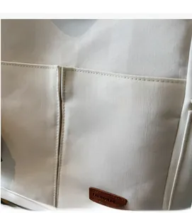 Detail of off-white canvas bag featuring double front pockets and brown leather logo patch