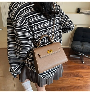 Detail of dark coffee leather handbag with lychee texture and gold metal twist lock buckle
