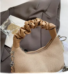 Close-up of beige woven seashell bag featuring a ruched leather handle and pearl chain