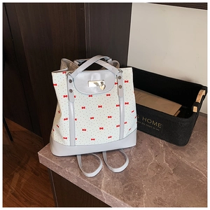 Detailed close-up of floral tote bag with red bow patterns and golden heart pendant