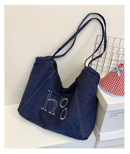 Detail of dark blue denim tote bag featuring white h g embroidery and long shoulder straps