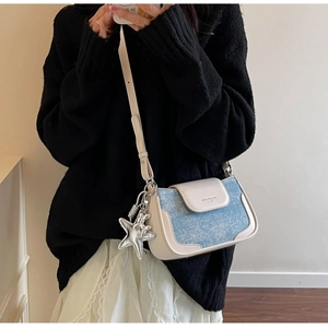 Detailed close-up of a blue denim and cream leather patchwork handbag with star charm