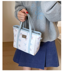 Detail view of cartoon bear print and metal logo plate on white leather bucket bag