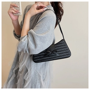 Detail of black woven shoulder bag with a bow accent worn by a model against a minimalist wall