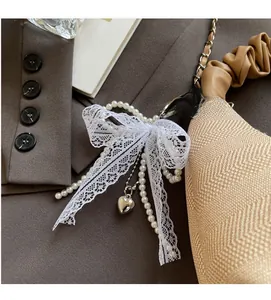 Detail of white lace bow charm with pearl bead chain and silver heart pendant on a bag