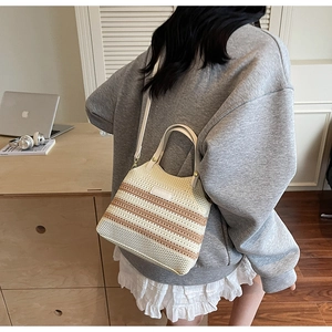 Detail of beige and brown striped knitted bucket bag worn by a model in a cozy study