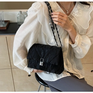 Detail of black quilted shoulder bag with silver metal buckle and chain strap on a model