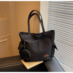 Detail view of black canvas tote bag with front pocket on leather sofa with shutters