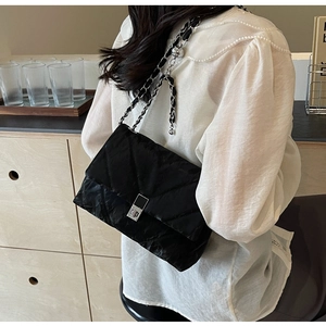 Close-up of black quilted shoulder bag with silver chain strap and metal turn-lock