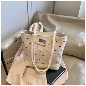 Close-up of white tote bag with red bow prints and silver heart charm on a chair