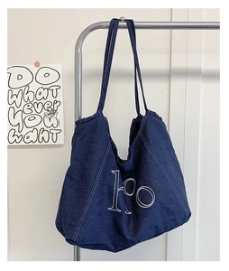 Close-up of a dark blue denim tote bag with ho letter embroidery on a hanger