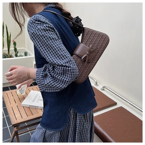 Detail of dark brown woven leather underarm bag with bow accent on a female model
