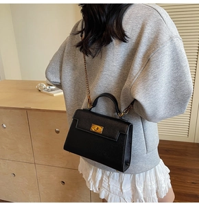 Detail of a black pebbled leather handbag with gold twist lock and metal chain strap