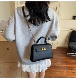 Detailed back view of a black structured Kelly bag with gold strap on model in home setting
