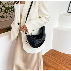 Détail d'un sac demi-lune noir en cuir brillant avec une chaîne à billes argentée