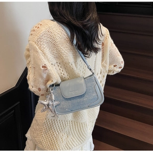 Detail of light blue glitter shoulder bag with silver star charm worn by a model