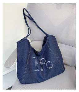 Detail of dark blue denim tote bag with white h°o embroidery on a grey mesh chair