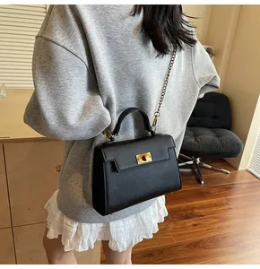 Detail of minimalist black saffiano leather bag with elegant gold twist lock and chain strap