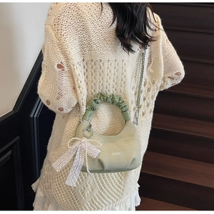 Detail of light green knit bag featuring ruched handle and white lace bow pearl charm