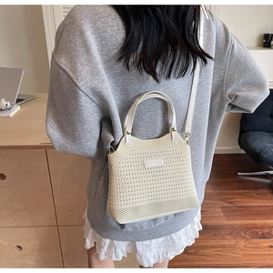 Detail view of beige knit bucket bag with white leather straps shown on a model