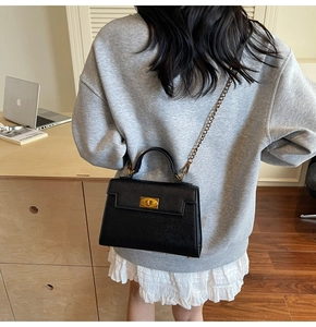 Detail of black lychee leather crossbody bag with gold twist lock on a model