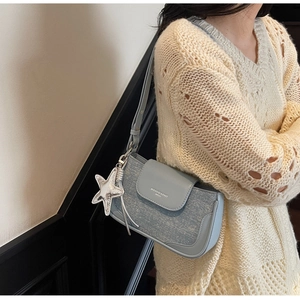 Detail of light blue shoulder bag featuring star charm and textured paneling for women