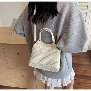 Detailed side view of a cream-white knitted bucket bag with leather handles and strap