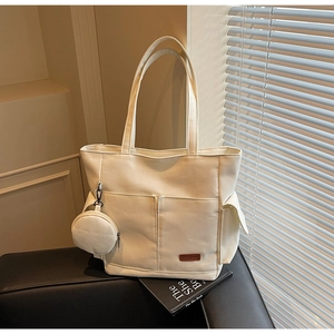 Detail of white canvas tote bag with front pockets and small round coin purse hanging on side