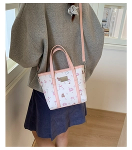 Detail of pink cartoon bear patterns and metal logo on a white tote bag held by a model