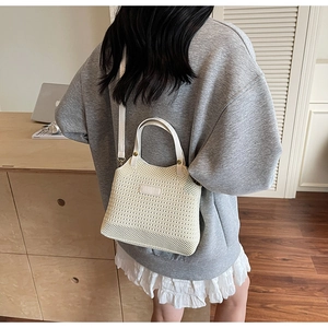 Detail of cream knit bucket bag with leather strap shown in a casual summer setting