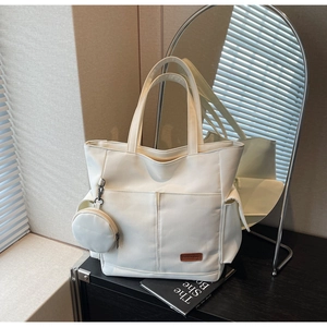 Detail of white canvas tote bag showing side flap pocket and round coin purse charm