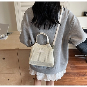 Detail of a creamy white woven bucket bag with top handle and adjustable shoulder strap