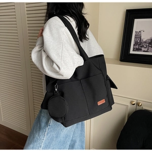 Detailed view of large black canvas tote bag with orange label and round coin purse charm