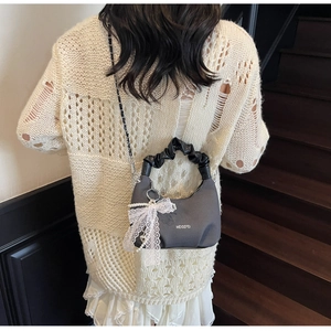 Gray textured handbag detail featuring white lace bow and elegant pearl charms