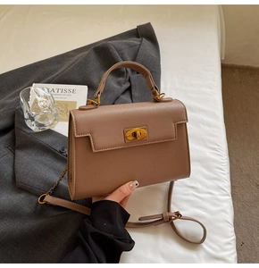 Detail of tan pebble leather handbag with gold oval twist lock on a casual setting