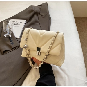 Detail of cream quilted chain bag with V-shaped stitching and silver ball charm