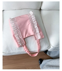 Detailed close-up of pink canvas tote bag with white lace trim on a white sofa
