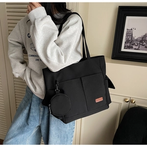 Detail of black canvas tote bag with orange fashion label and round coin purse pendant