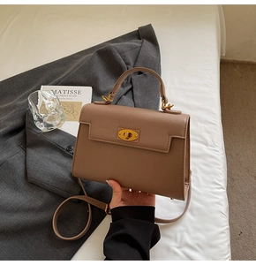 Detail of tan textured leather handbag with gold twist lock and adjustable shoulder strap