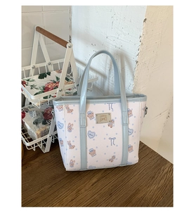 Close-up of the metal logo plaque and cartoon prints on the light blue leather bucket bag