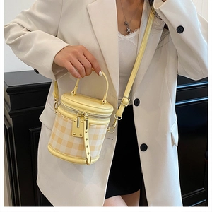 Detail of yellow quilted cylinder bag with handle and detachable shoulder strap on model