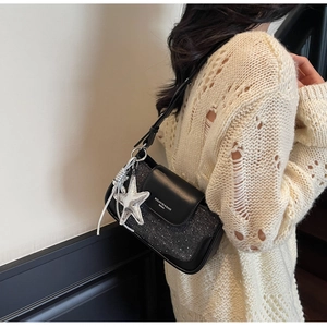Detail of a chic black square bag with a silver star charm and adjustable strap