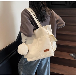 Close-up of cream canvas tote bag showing functional outer pockets and small round coin purse