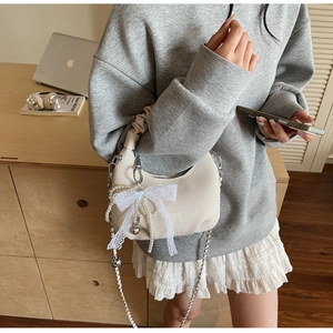 Detail of cream crescent bag with layered pearl chains and oversized lace bow charm