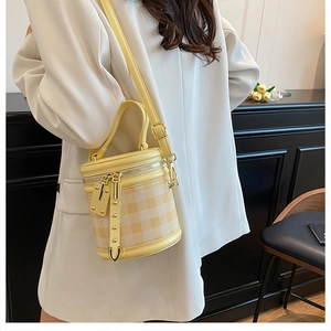Detail of yellow checkered bucket bag with gold rivets and adjustable shoulder strap