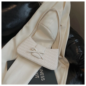 Detail of white woven baguette bag with bow decoration on a white blazer background