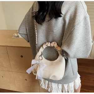 Close-up of white pleated dumpling bag featuring lace bows and pearl chain accessories