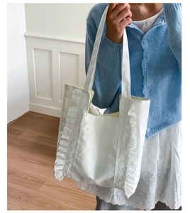 Detail view of a white canvas tote bag with lace trim decorations and wide shoulder straps